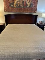 Full view of California king mahogany stained bed frame and mattress with a curved headboard and neutral beige quilted bedspread