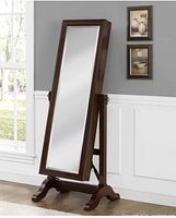 Full-length dark wood freestanding jewelry cabinet with tilt mirror door shown angled in a room against a wall and window.