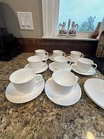 Full set of 8 white Wedgwood teacups and 10 matching saucers arranged on countertop
