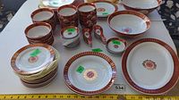 Full view of stacked plates, small bowls, medium bowls, and spoons showing uniform red and gold Asian themed design and motifs