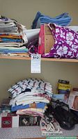 Shelf with stacks of various folded tea towels, cloths and a purple floral bag containing textiles.