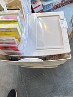 Top view of white plastic storage bin partially open showing boxes of greeting cards inside.