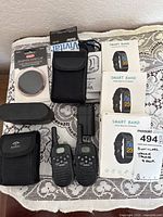 All items laid out including binoculars with strap and case, two walkie-talkies, lens cap in package, smart bands boxed, and carrying cases.