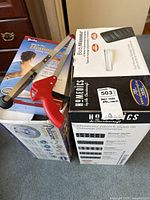 Boxes and items stacked including the BodyMasseur massage mat box, pedicure foot spa box, heating pad box, and assist aid reach tool visible on top.