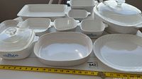 Overview of Corningware casserole dishes and serving pieces in white with blue cornflower design with glass lids and Corelle serving plate.