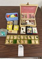 Overview of assorted costume jewelry and accessories arranged on a table, including small boxes and a beige display box with pink velvet lining.