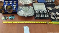 Full lot display of silverware, goblets, trays, and napkin rings alongside measuring tape for scale