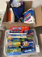 Top-down view of an open box containing a large roll of Scott paper towels, spray cleaner bottles, and reusable blue organizer holding smaller items.