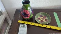 Green Moorecroft vase and small floral plate with a measuring tape showing vase height about 5.5 inches