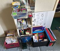 Front view of small wooden shelf unit with office supplies and bins containing various items including rubber bands, sticky notes, envelopes, and binders.