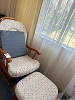 Overall view of wooden rocking chair with matching ottoman and gray lumbar pillow near window