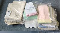 Overview of multiple stacks of linens and napkins in plastic bags showing pastel colors and embroidery