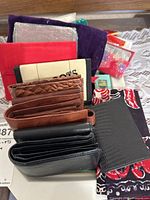 Photo showing stacked wallets of various materials including leather and fabric with some colorful smaller wallets in the background.