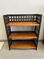 Front view showing 3-tier short bookcase with black framed grid sides and dark golden brown wooden shelves.