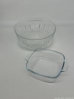 Round glass bowl with starburst and faceted pattern next to square glass dish with handles on a plain background.