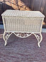 Front view of natural color wicker side table showing rectangular lid and scrollwork legs.