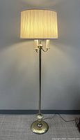 Full view of brass floor lamp with cream fabric shade showing lamp base and height