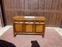 Front view of vintage buffet cabinet showing three drawers and three cabinet doors with burled wood inlay, stone top insert visible.