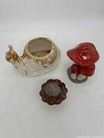 Snail planter pot with two red ceramic mushrooms and small round flower-shaped ceramic object shown together.