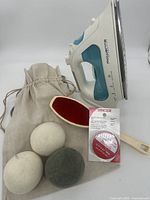 Rowenta steam iron, wool dryer balls in bag, lint brush, and Singer fabric tape grouped together on white background.