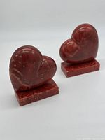 Pair of red heart-shaped alabaster bookends on a white background, showing their size and shape.
