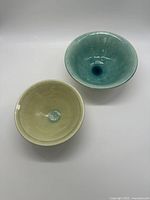 Top-down view of two handmade pottery bowls, one pale green and one turquoise blue, showing interior details and glaze.