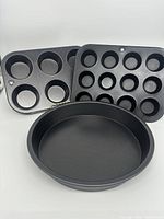 Two metal muffin pans (one standard 6 cups and one mini 12 cups) with a 9-inch round cake pan in black non-stick metal.