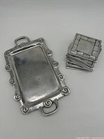 Small rectangular silver toned decorative tray with ornate curled edge detail and handles, resting flat on surface.