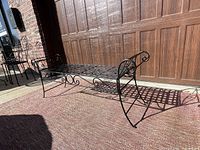 Side view of outdoor wrought iron bench showing basket weave seat and scroll arms