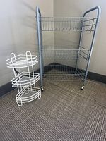 Photo showing both the small white metal corner shelf and the light blue 3-tier rolling cart side by side against a wall on carpeted floor.
