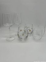 Four short stemless wine glasses, two with colored polka dots in silver, gold, purple, and two plain clear stemless wine glasses shown on a white background
