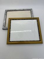 Two metal photo frames, one silver 8x10 and one gold-tone with decorative edge 5x7, showing frame condition and surfaces.