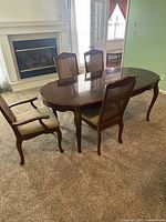 Dining table with four cane-back chairs in a room near fireplace. The table has a polished wood surface with slight scratches. One arm chair and three side chairs with cane backs are around the table.