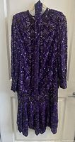 Front view of purple sequin drop-waist dress with long sleeves on hanger.