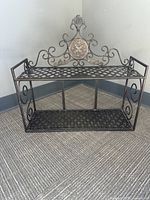 Front view of the wrought iron 2-tier decorative wall shelf showing lattice shelves, ornate scrollwork, and floral medallion