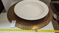 Top-down view of white ceramic bowl/platter set inside large brass tray with measuring tape showing the tray's approximate size of 27 inches.