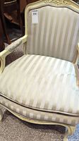 Front and angled views of a single beige striped upholstered armchair with carved wood frame painted distressed cream.