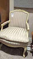 Front angle of the wood framed armchair with striped cream and beige upholstery. Visible carved floral details on the wooden frame.