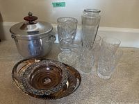 Photo showing 4 tall crystal glasses, 1 crystal vase, 4 crystal coasters arranged near a silver ice bucket with a wooden knob lid and a Birks oval silver plate with ornate silver-plated bottle holder in front.
