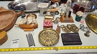 Photo of various decor items including metal trays, wooden bowls, brass tray, leather wallet, model ship, brass horse heads, and other small decorative pieces