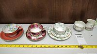 Overview of three fine china teacup and saucer sets with milk jug and creamer on a shelf