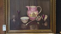 Framed oil on canvas painting showing pink jug with sailing ship motif, two bowls, metal ladle, and purple glasses in still life.