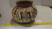 Full view of the round woven grass basket showing bird motif and size comparison with yellow scale ruler