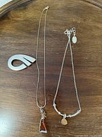 Two silver necklaces with distinct pendants shown alongside a modern abstract silver brooch.