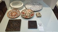 Set of decorative marble bowls, marble lazy Susan, brass enamel bowls, small decorative box, and stone coasters placed on a white surface