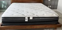 View of mattress on bed frame showing quilted white top and black sides with Beautyrest tag in like new condition.