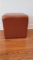 Front view of EQ3 leather cube ottoman showing its cube shape and orange/brick leather upholstery.