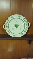 Round white porcelain platter with two handles, green floral decoration and gold trim against a wooden background
