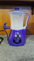 Front view of purple Cadbury hot chocolate maker with clear container and spout. Control knob visible on front base.