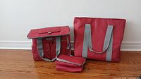 Overview showing all three insulated bags: large tote, medium flap bag, and small rectangular bag, all red with grey handles on wooden floor.